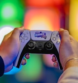 Two hands are holding a gaming controller labeled 'Pro Gamer'. The background is blurred with colorful lights creating a vibrant atmosphere.