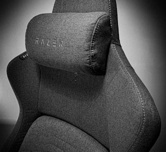 A high-quality, fabric gaming chair featuring ergonomic design and enhanced comfort. The chair has a distinct headrest with visible stitching, embossed branding, and a modern aesthetic.