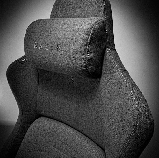 A high-quality, fabric gaming chair featuring ergonomic design and enhanced comfort. The chair has a distinct headrest with visible stitching, embossed branding, and a modern aesthetic.
